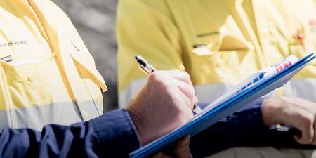 Close shot of mid-section of two Resources Regulator staff - one is writing on a clip board.